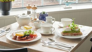 Une table de petit-déjeuner dressée avec des assiettes remplies de nourriture, des tasses et des couverts.
