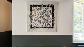 Un comedor con una mesa y sillas de madera, una obra de arte abstracta en la pared y una ventana con vistas a la vegetación.