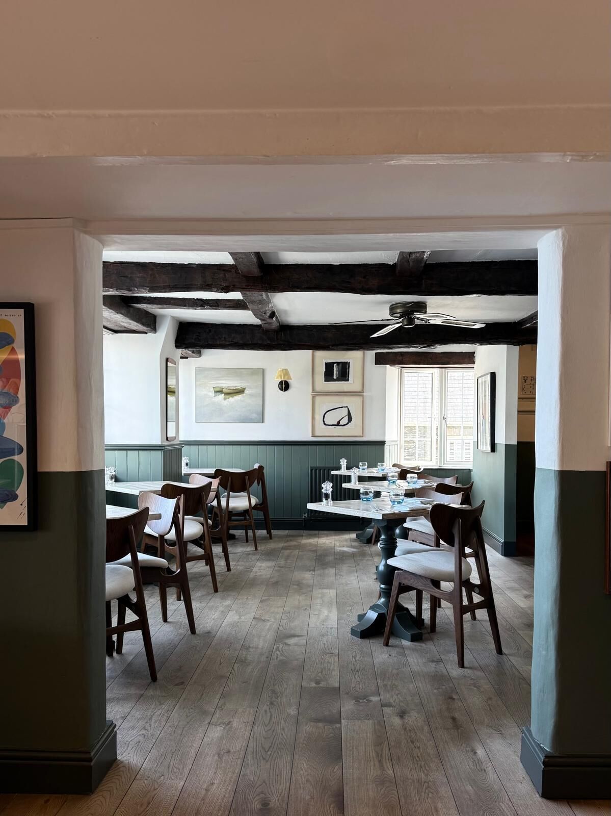 A dining area with wooden tables and chairs, a ceiling with exposed beams, and artwork on the walls.