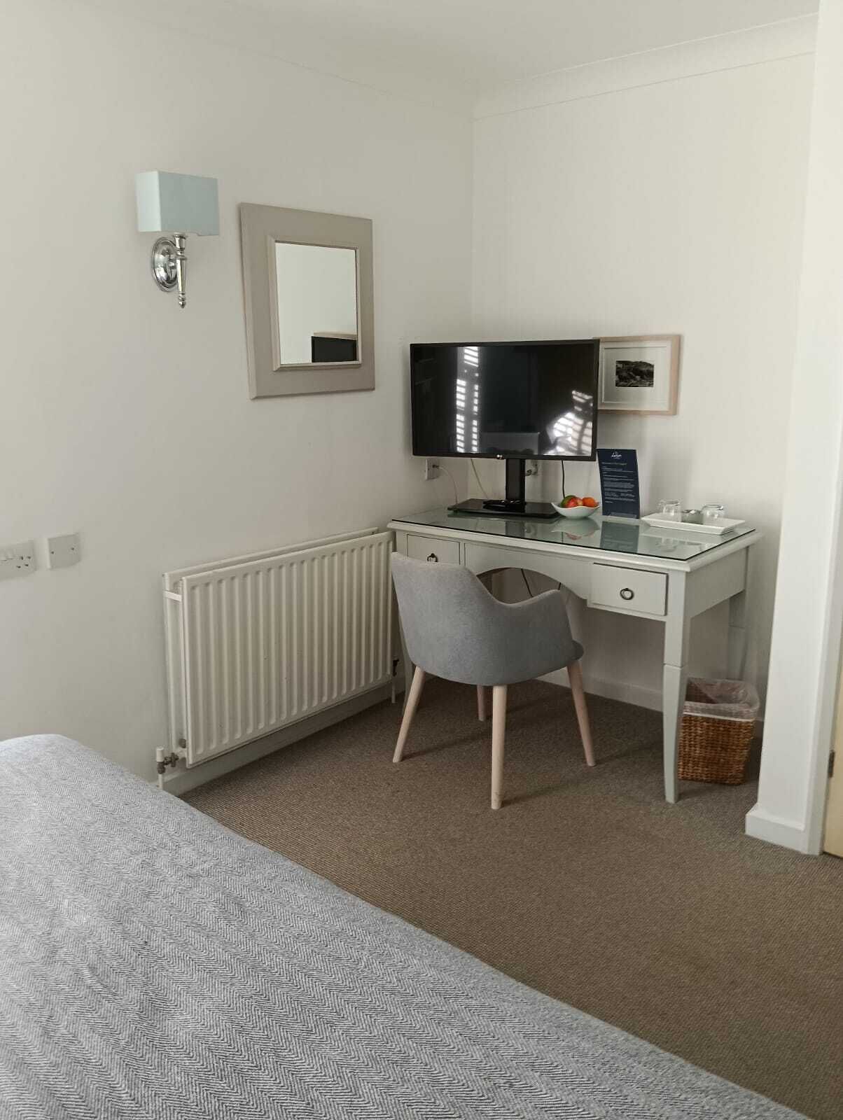 A bedroom with a bed, a desk with a computer, a chair, a radiator, and a small picture frame on the wall.
