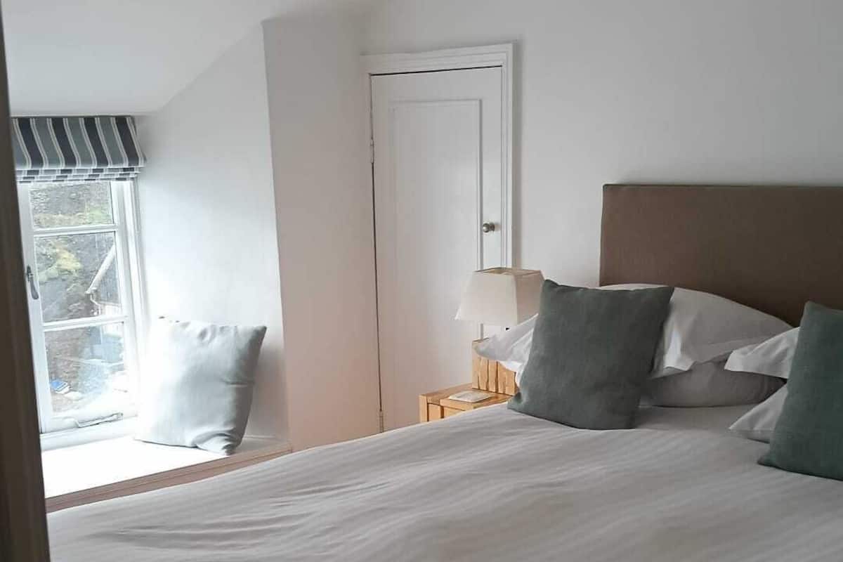 Un dormitorio con una cama grande, una mesita de noche con lámpara, una ventana con vistas y una puerta.