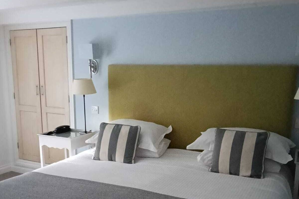 Una habitación de hotel con una cama grande, dos mesitas de noche, una lámpara y un armario.