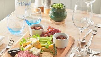 Una mesa de madera con una variedad de quesos, galletas y uvas, junto con una botella de agua y copas de vino.