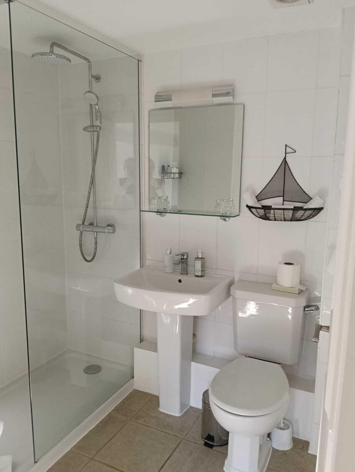 Ett modernt badrum med en dusch som är avskärmad med glasväggar, ett vitt handfat och en toalett.