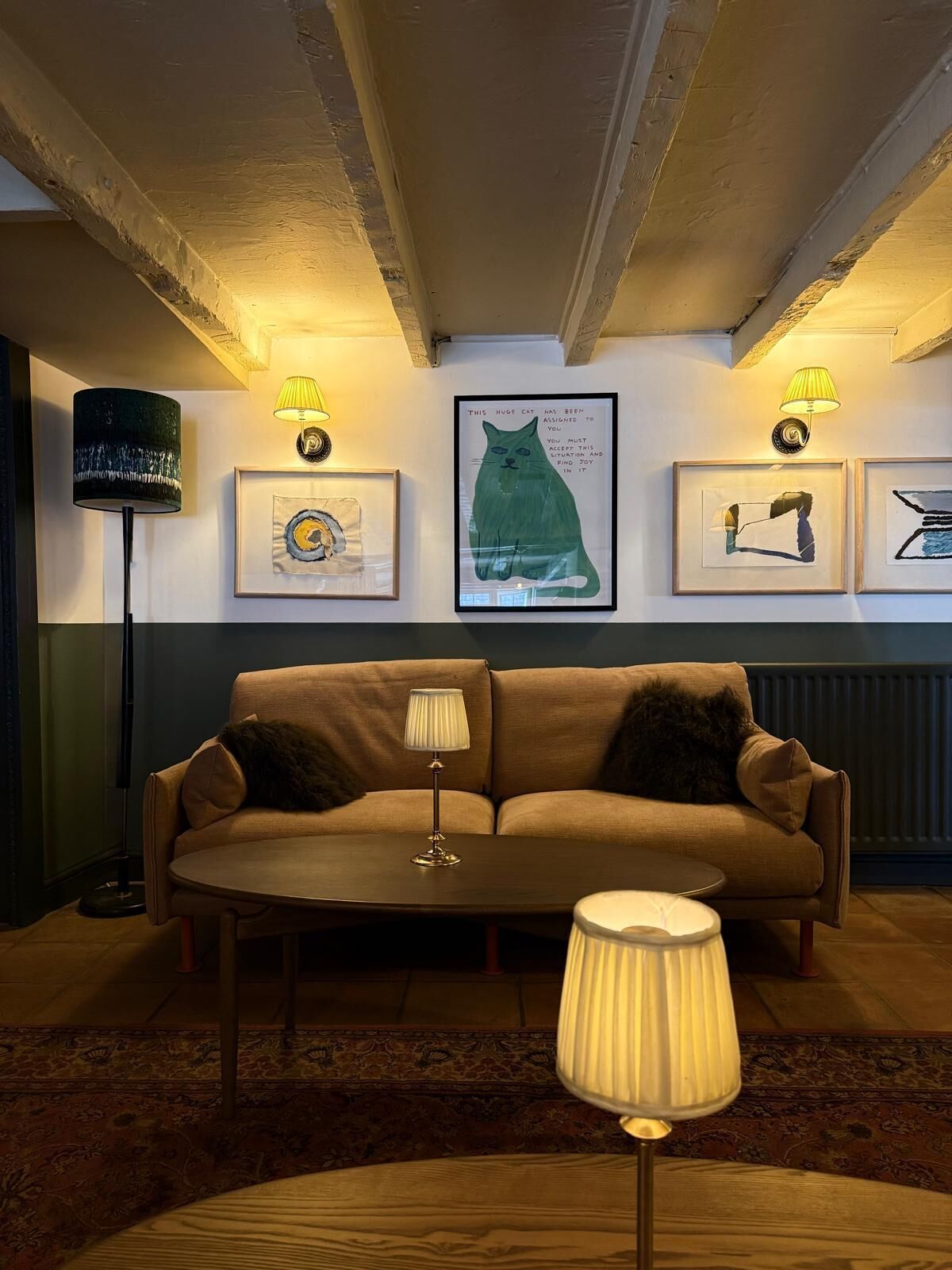 A cozy living room with a sofa, a coffee table, and a lamp. There are framed artworks on the wall.