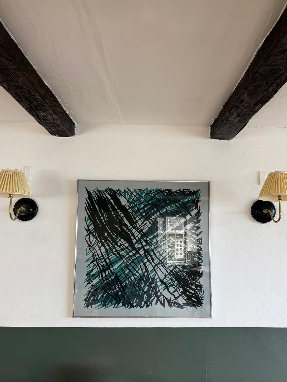 Una habitación con un cuadro abstracto grande en la pared, dos lámparas fijadas a la pared y vigas de madera a la vista.