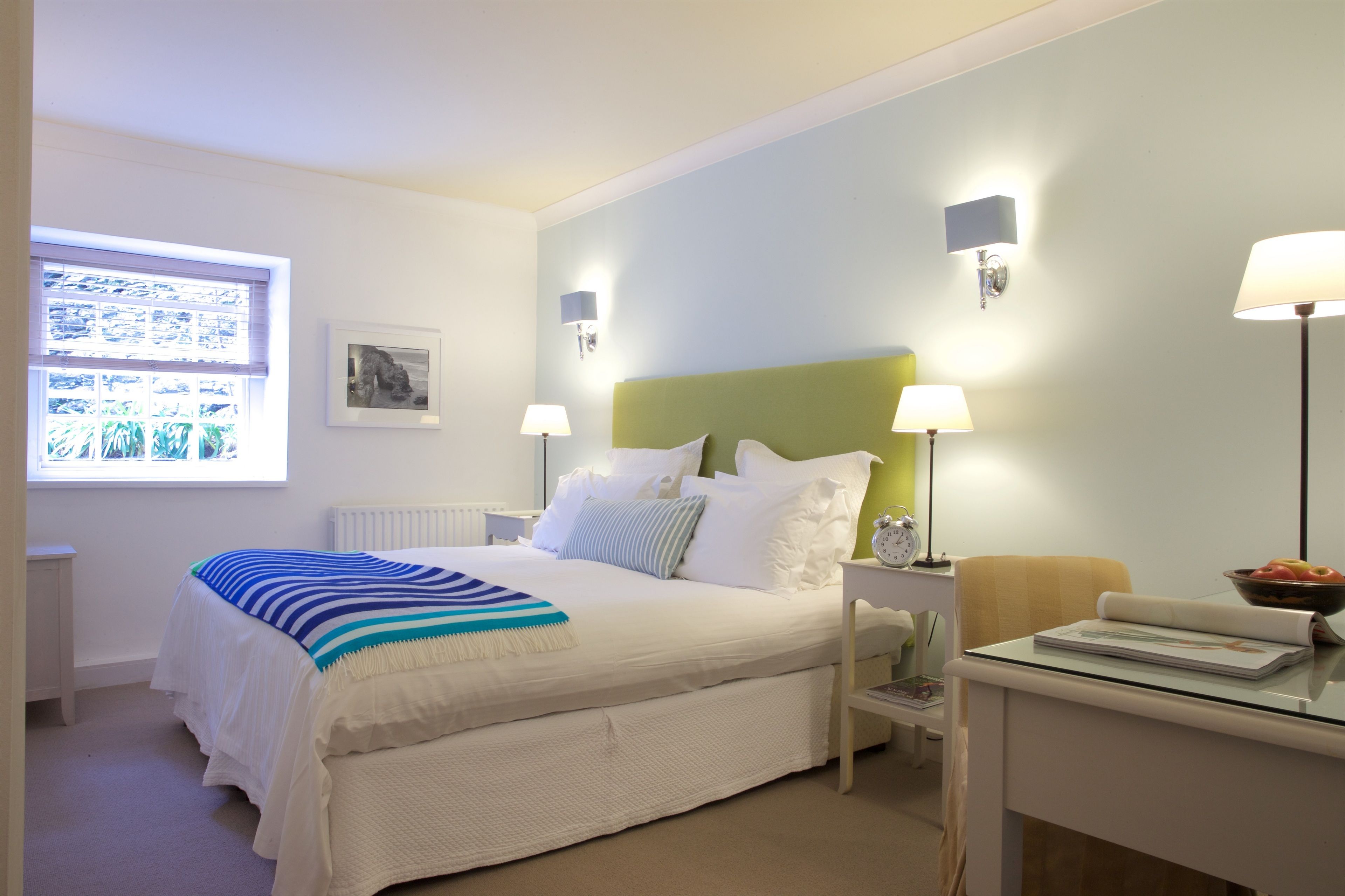 A neatly arranged bedroom with a bed, bedside lamps, a nightstand, a chair, and a window with blinds.