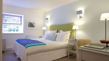 A neatly arranged bedroom with a bed, bedside lamps, a nightstand, a chair, and a window with blinds.