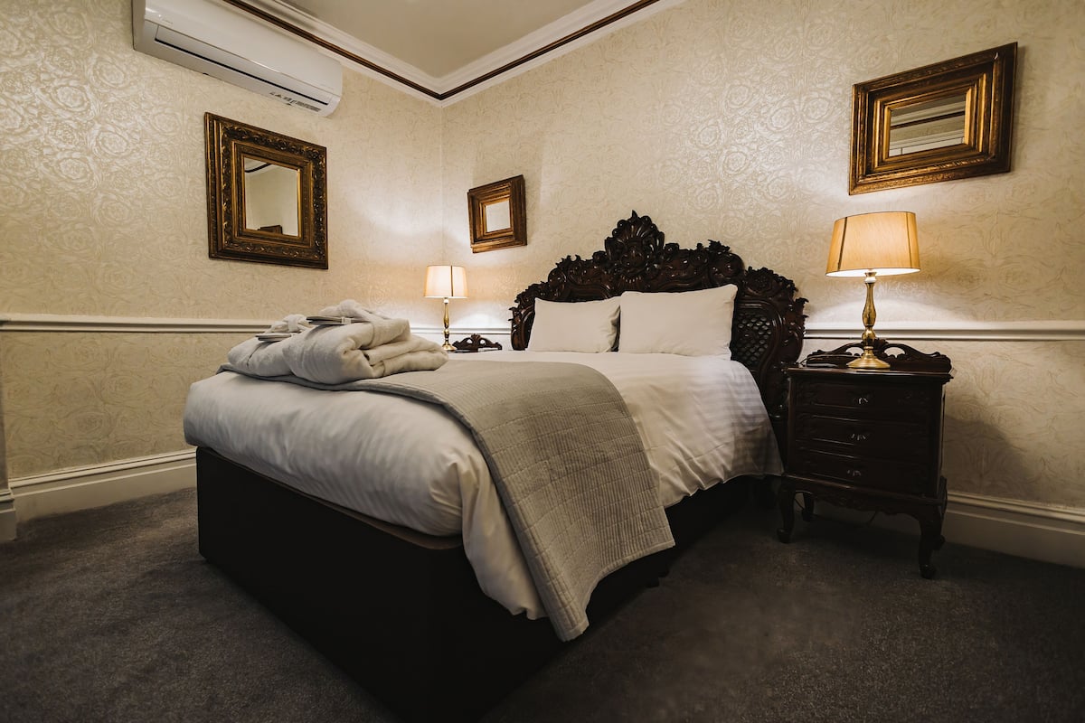 A hotel room with a large bed, a bedside table with a lamp, and two wall-mounted mirrors.