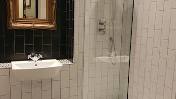 Un baño con un lavamanos blanco, un espejo con un marco decorativo y una ducha con puerta de vidrio.