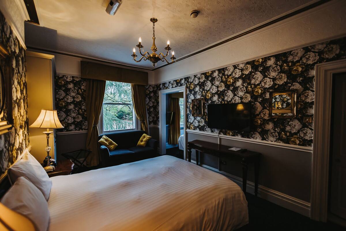 A hotel room with a large bed, a desk, a chair, a TV, and a window with curtains.