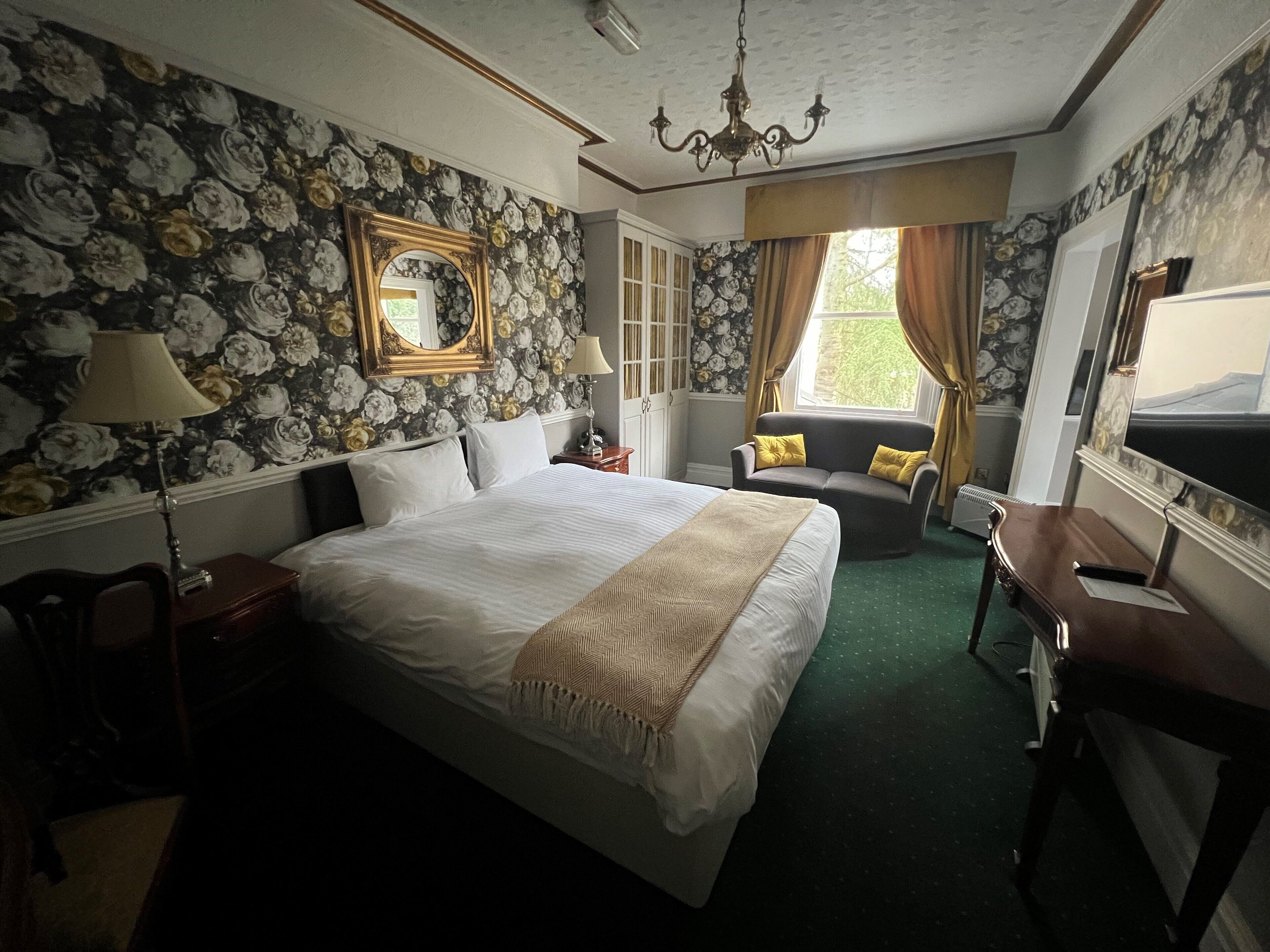 Habitación de hotel con una cama grande, un sofá, un escritorio y una ventana con cortinas.