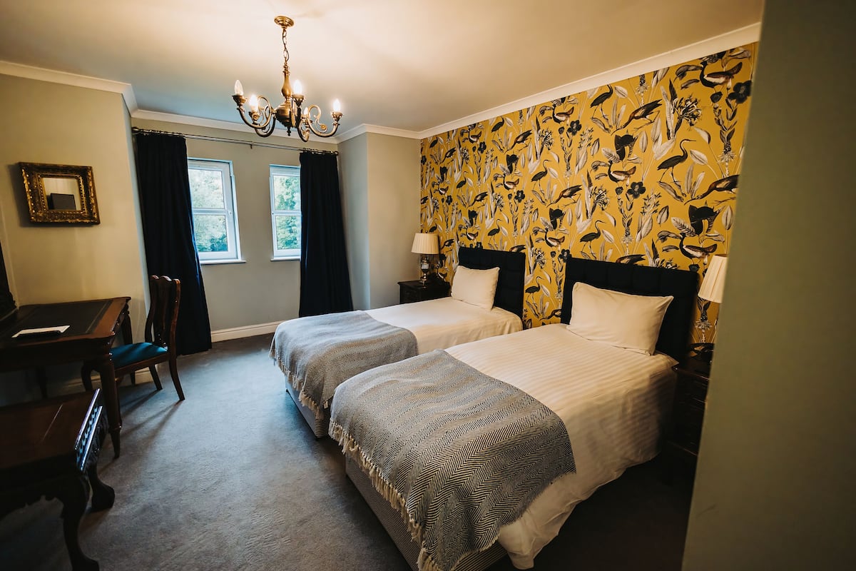 A hotel room with two beds, a desk, a chair, and a chandelier.