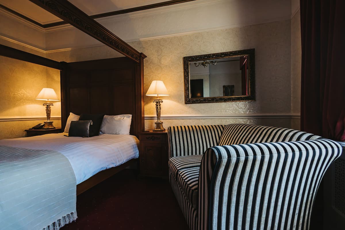 A hotel room with a bed, two bedside tables with lamps, a striped armchair, and a mirror on the wall.