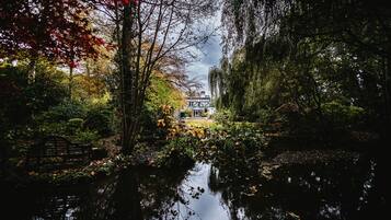 A serene riverside setting with a traditional house, a wooden bench, and lush foliage.
