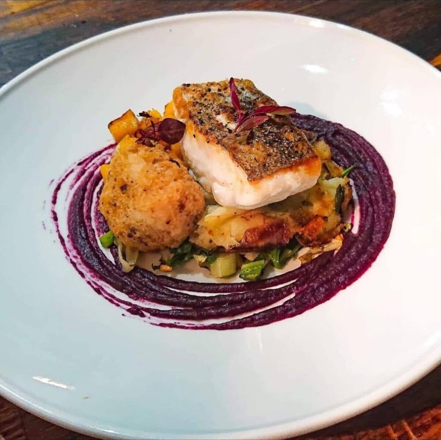 Un plato con un trozo de pescado, un pan redondo y una salsa morada.