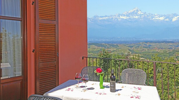 A balcony with a table set for two, a bottle of wine, and a vase with a flower. - Al Brich (Albaretto della Torre)