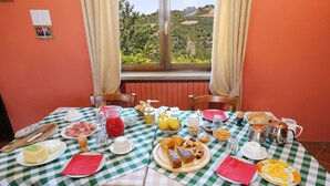 A breakfast table set with various food items, a view of the countryside through a window, and a checkered tablecloth. - Al Brich (Albaretto della Torre)