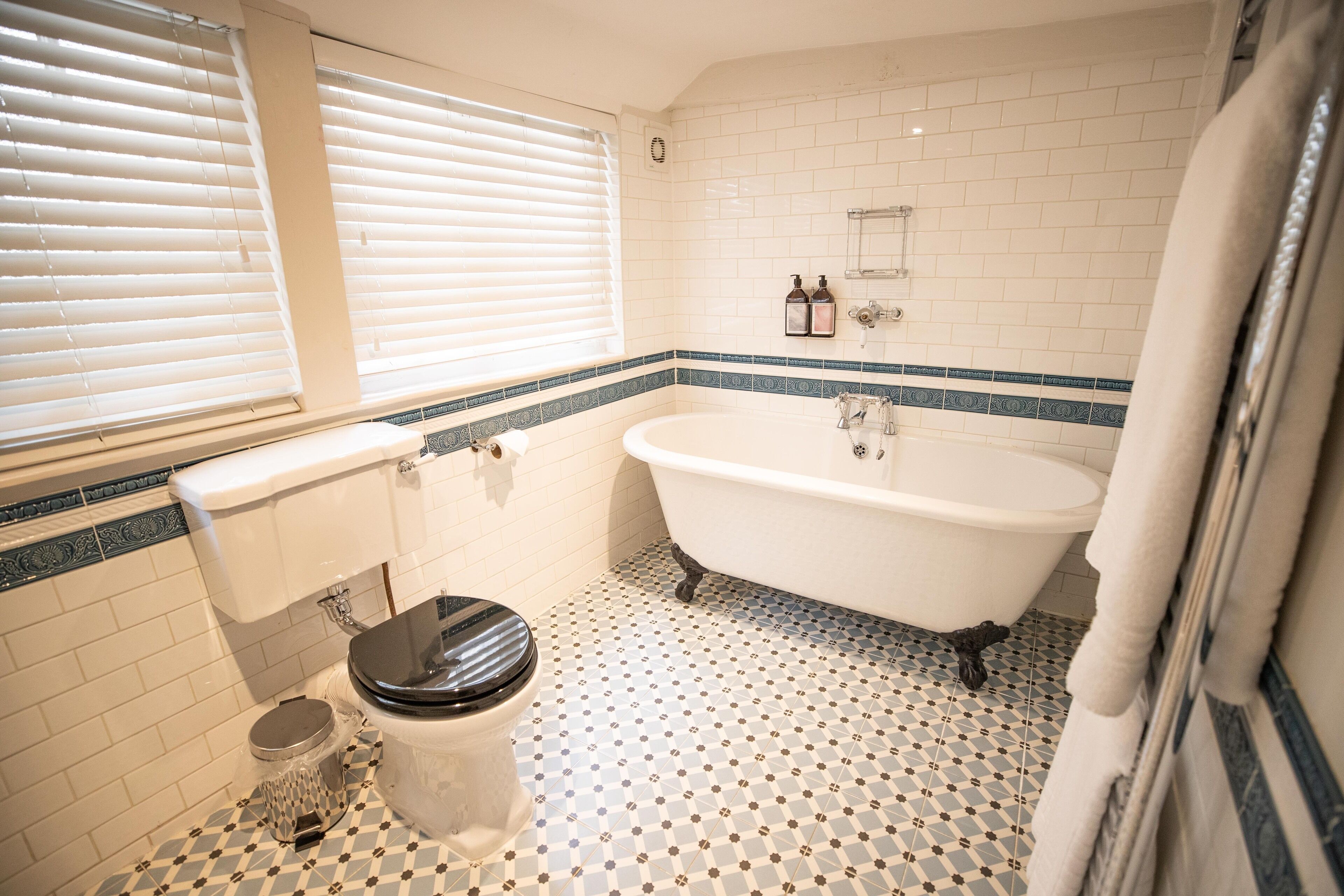 A bathroom with a white bathtub, a toilet, and a window with blinds.