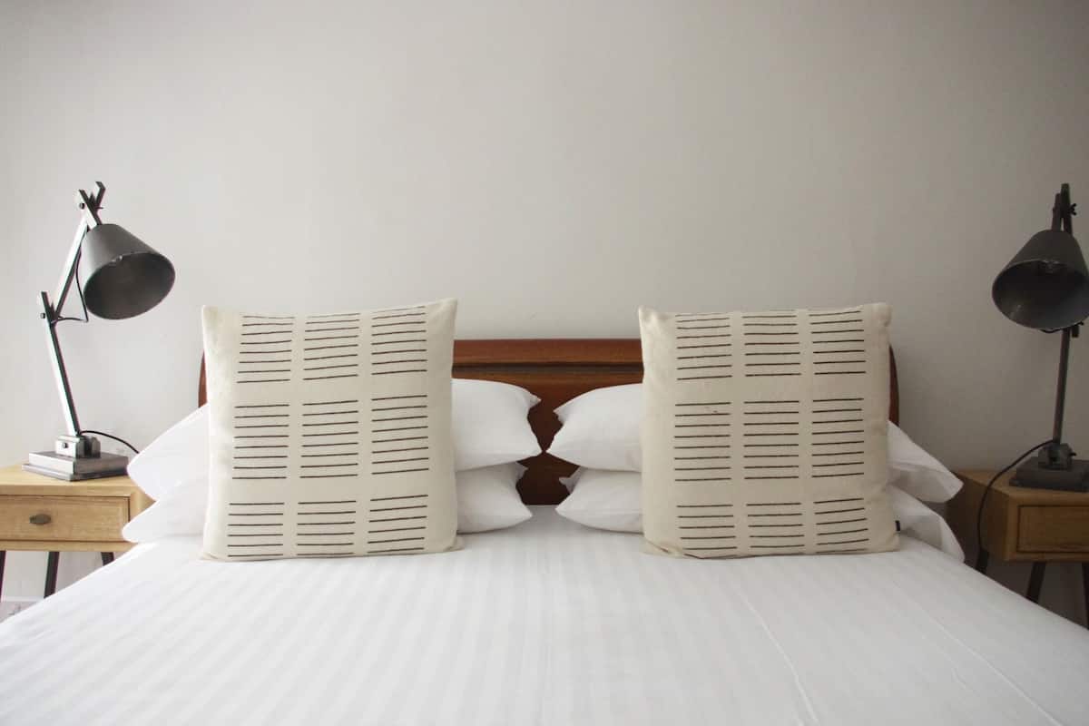 A neatly made bed with two pillows, a wooden headboard, and two bedside lamps on wooden nightstands.