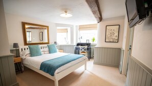 Un dormitorio con cama, escritorio, silla, espejo y televisor.