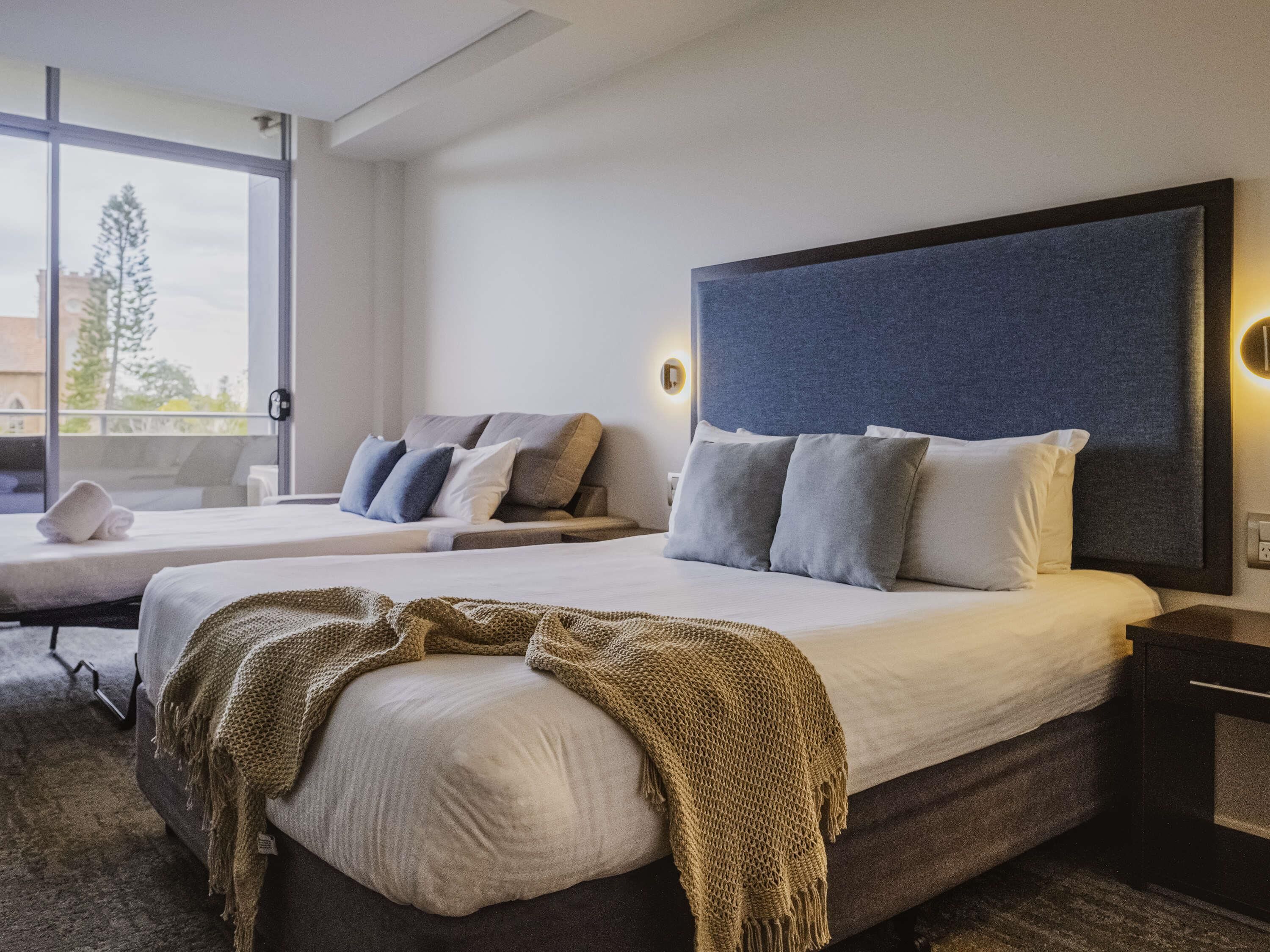A hotel room with two beds, a large window, and a view of the outdoors.