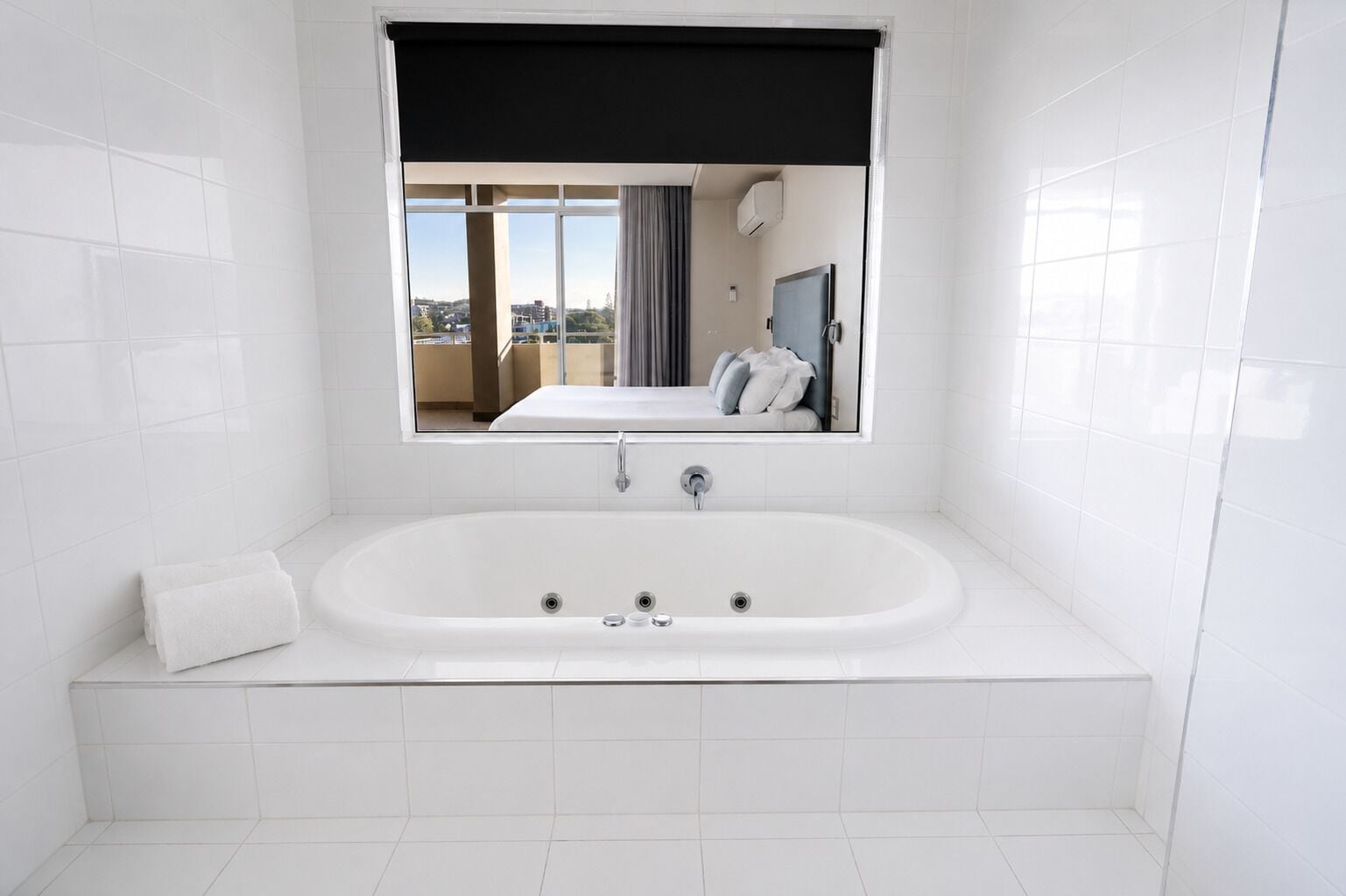 A modern bathroom with a large bathtub, a window with a view of the city, and a mirror above the tub.