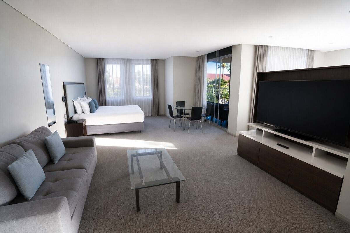 A modern hotel room with a bed, sofa, TV, and a balcony with a view.