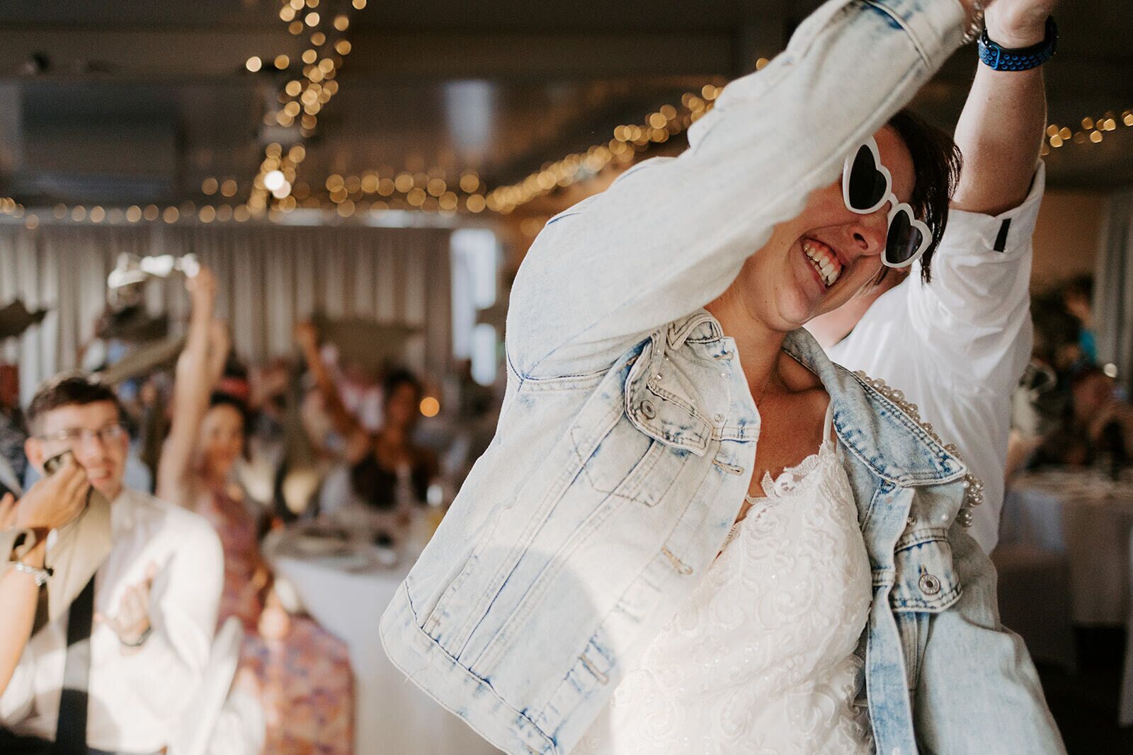 A person in a white shirt and denim jacket, raising their arms in a celebratory gesture.