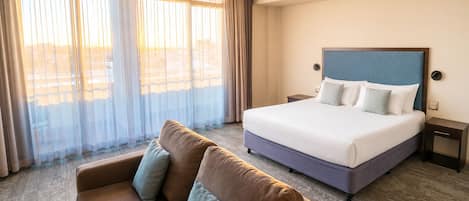 A hotel room with a bed, a sofa, and a large window with curtains.