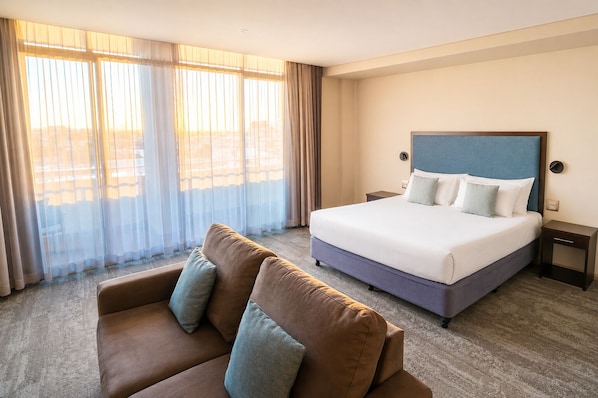 A hotel room with a bed, a sofa, and a large window with curtains.