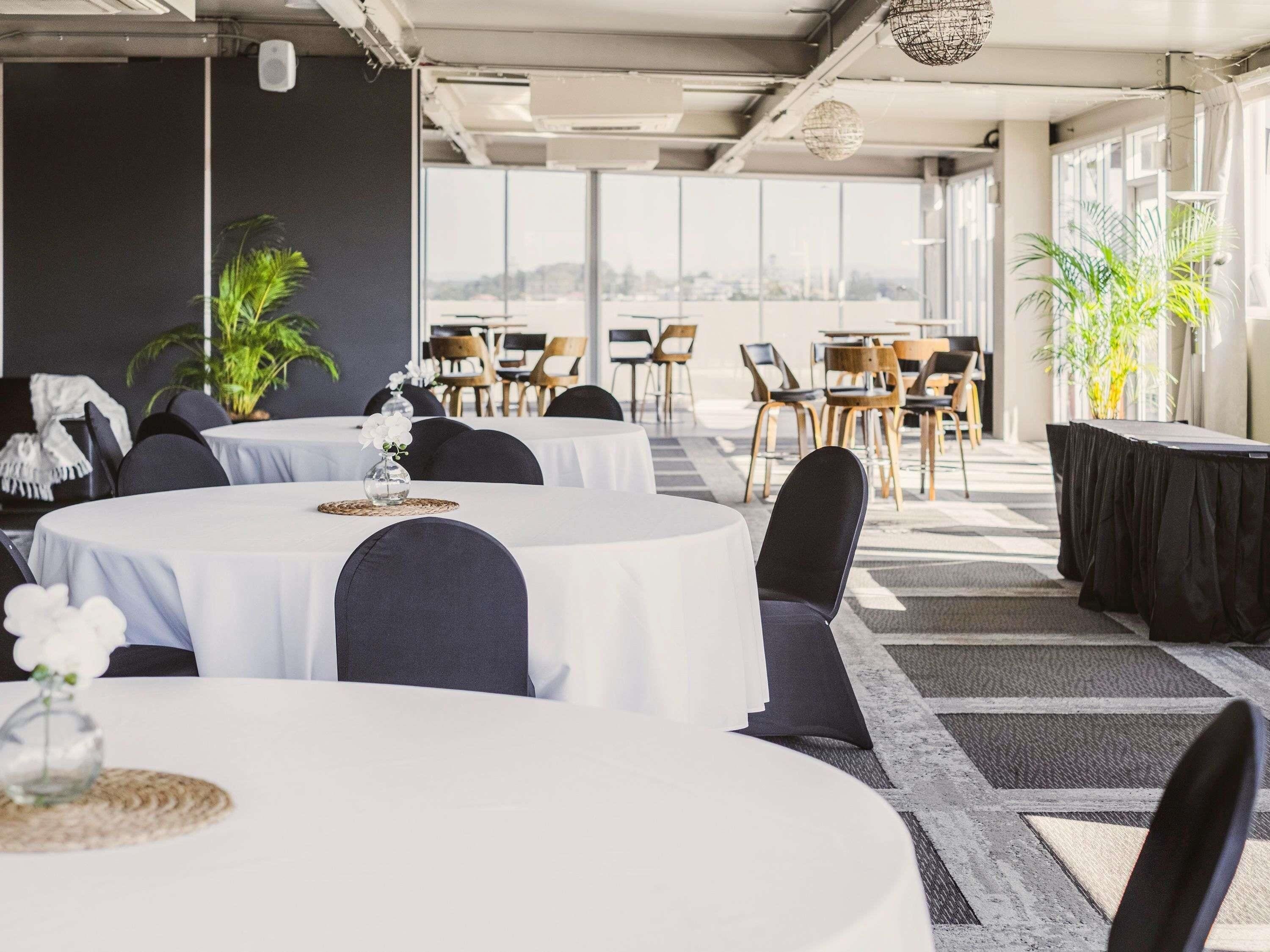 A conference room with round tables, black chairs, and potted plants.