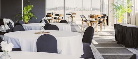 A conference room with round tables, black chairs, and potted plants.
