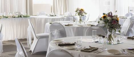 A banquet hall with round tables set for dining, white chairs, and a chandelier.