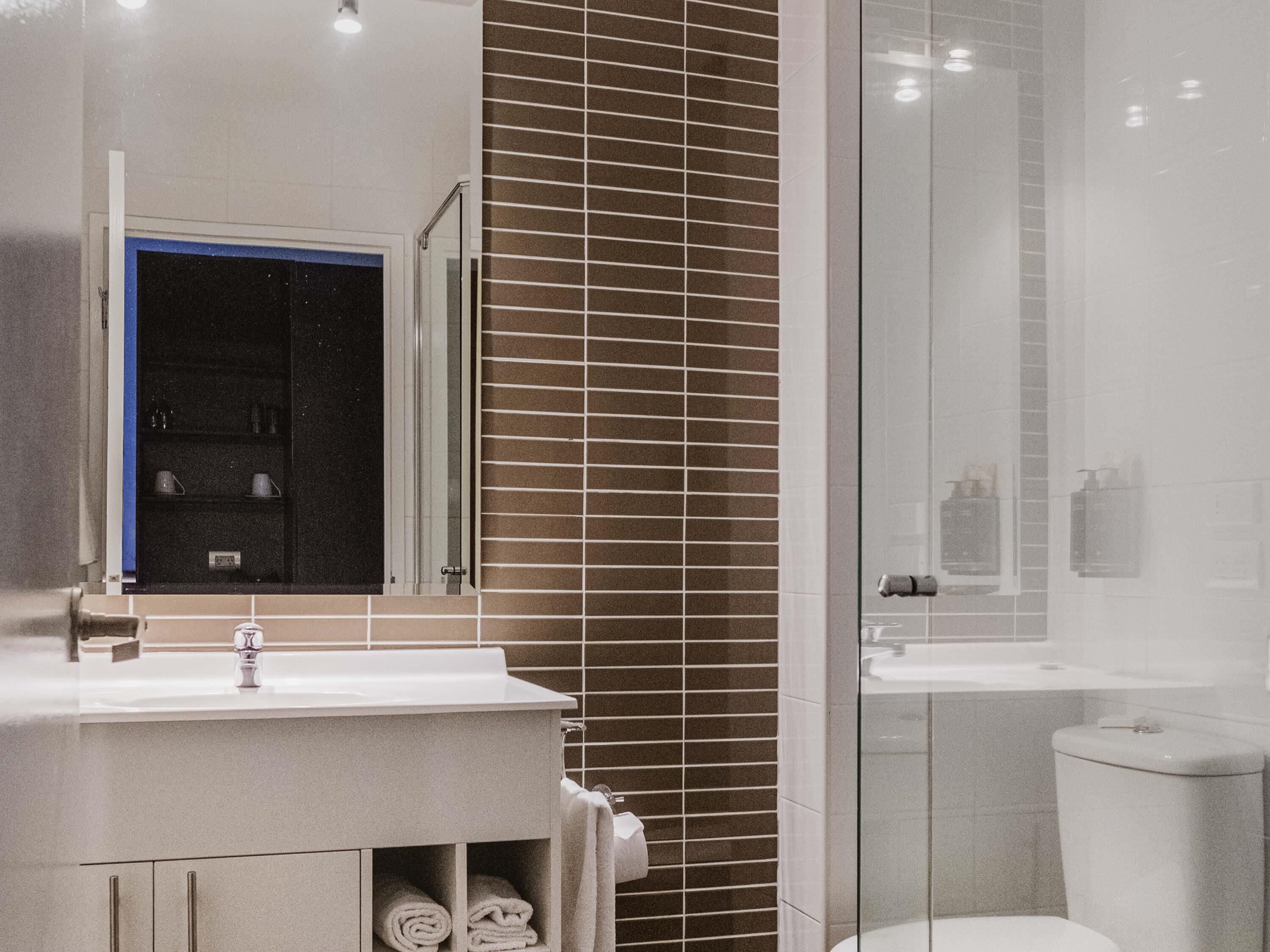 A bathroom with a white sink, a mirror, a glass shower enclosure, and a toilet.