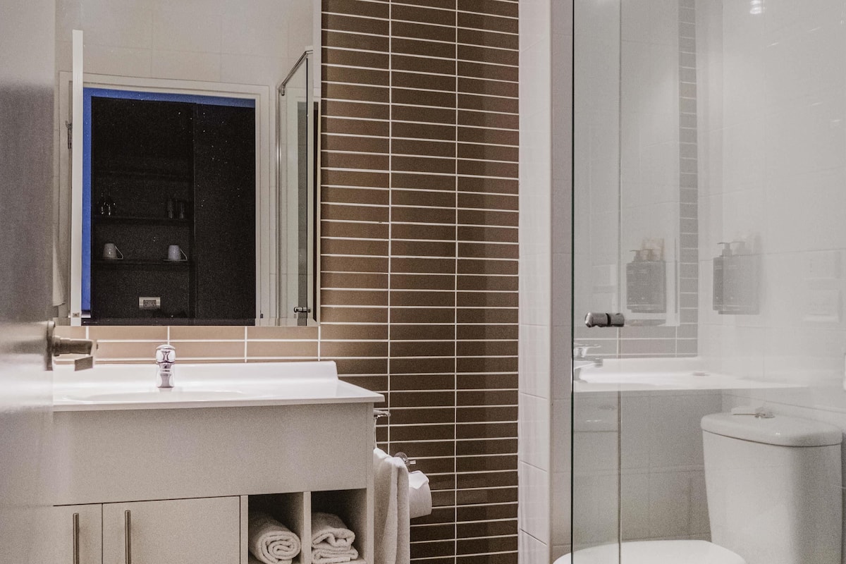 A bathroom with a white sink, a mirror, a glass shower enclosure, and a toilet.