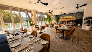A restaurant with multiple tables, chairs, ceiling fans, and a large window providing a view of the outdoors.