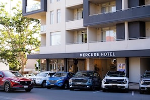 A hotel with multiple floors, a sign reading 'Mercure Hotel,' and several parked cars in front.