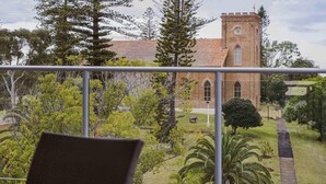 A balcony with a view of a brick building with a clock tower, surrounded by greenery and trees. - Mercure Centro Port Macquarie (Port Macquarie)