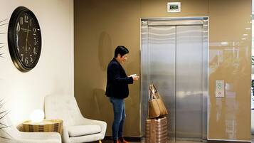 A hotel lobby with a clock, a waiting area with chairs, and an elevator.