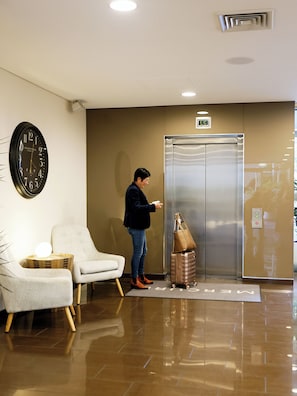 A hotel lobby with a clock, a waiting area with chairs, and an elevator.