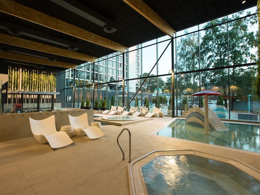 Un área de piscina interior con sillones modernos, un jacuzzi y vistas al exterior a través de amplios ventanales.