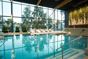 An indoor swimming pool with clear glass walls, lounge chairs, and a view of trees outside. - Hotel Jurmala Spa & Conference Center (Jurmala)