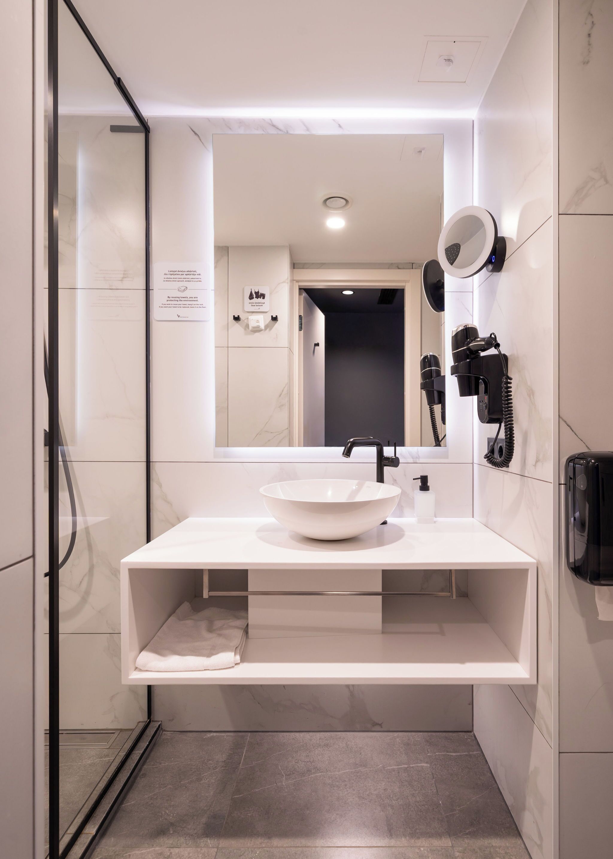 Moderni kylpyhuone, jossa on valkoinen pesuallas, suuri peili ja seinälle asennettu hiustenkuivaaja.