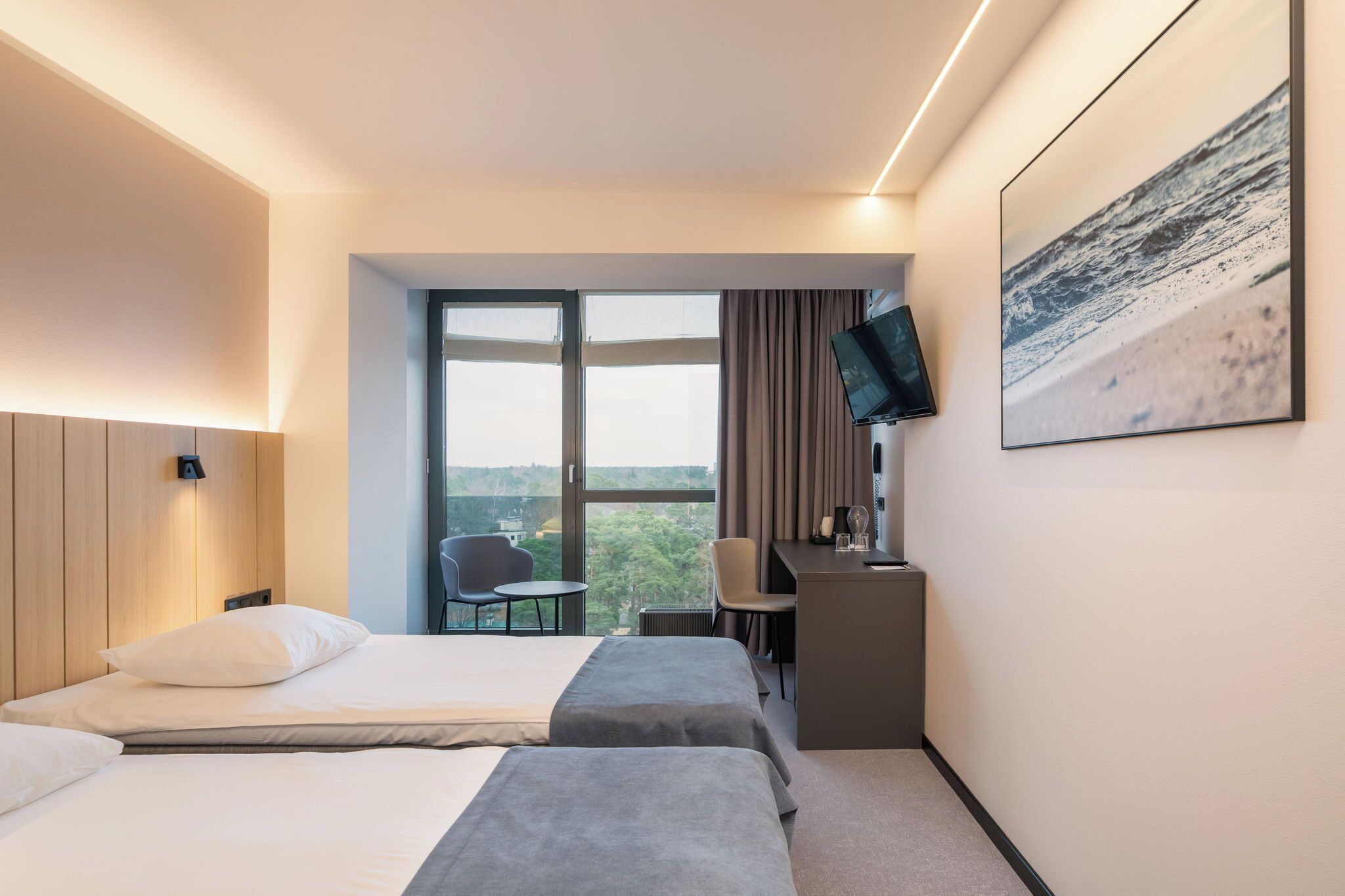 Hotelkamer met twee bedden, een bureau, een stoel, een televisie en een groot raam met uitzicht.