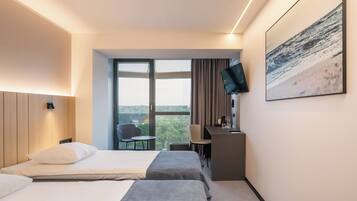 Hotelkamer met twee bedden, een bureau, een stoel, een televisie en een groot raam met uitzicht.