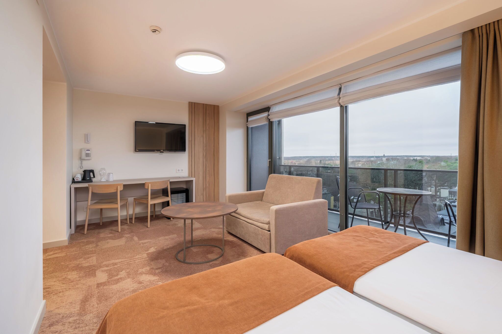 Habitación de hotel con cama, escritorio, silla, una mesita y un ventanal grande con vista a la ciudad.