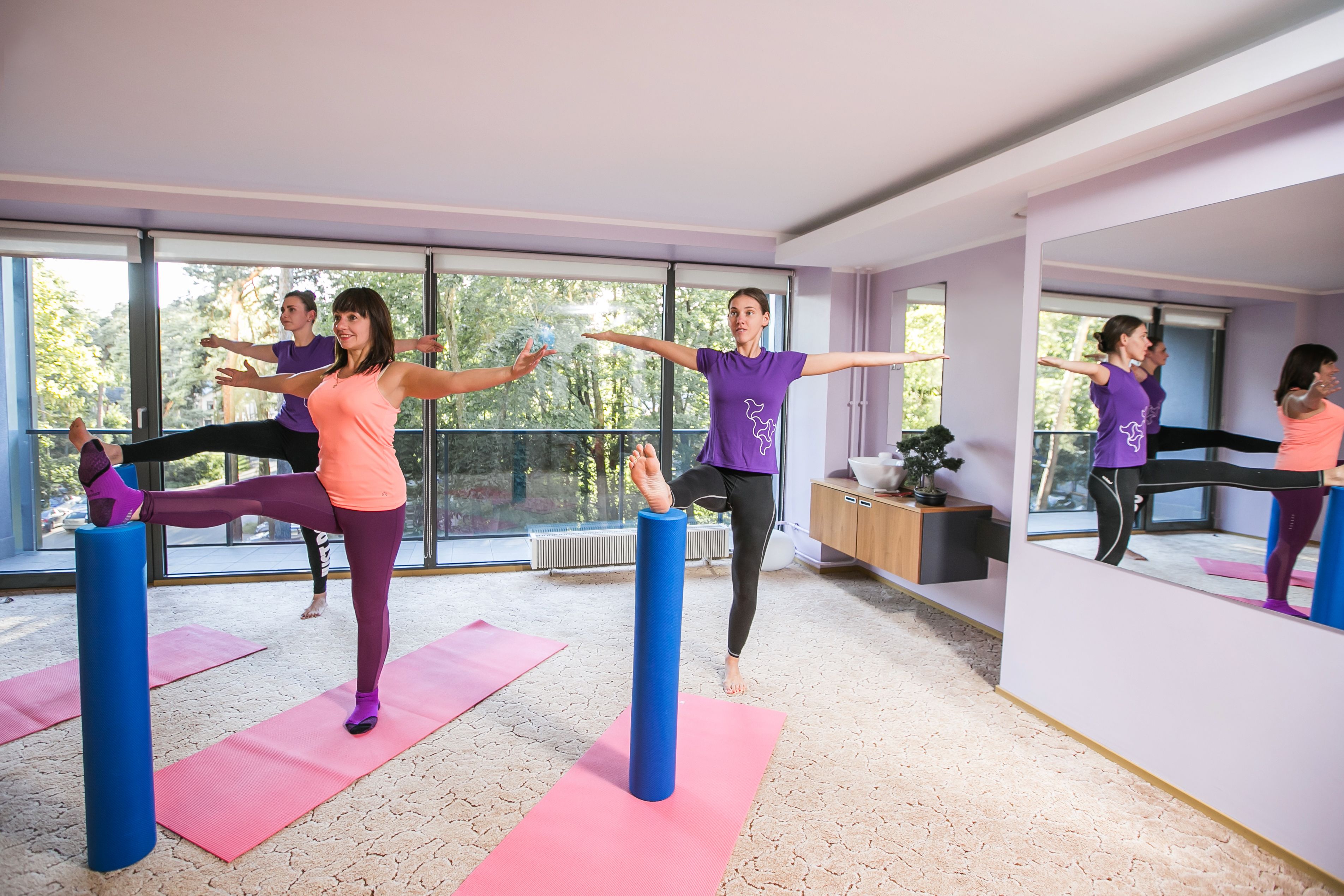 A yoga class in a modern room with large windows, yoga mats, and blue yoga blocks.