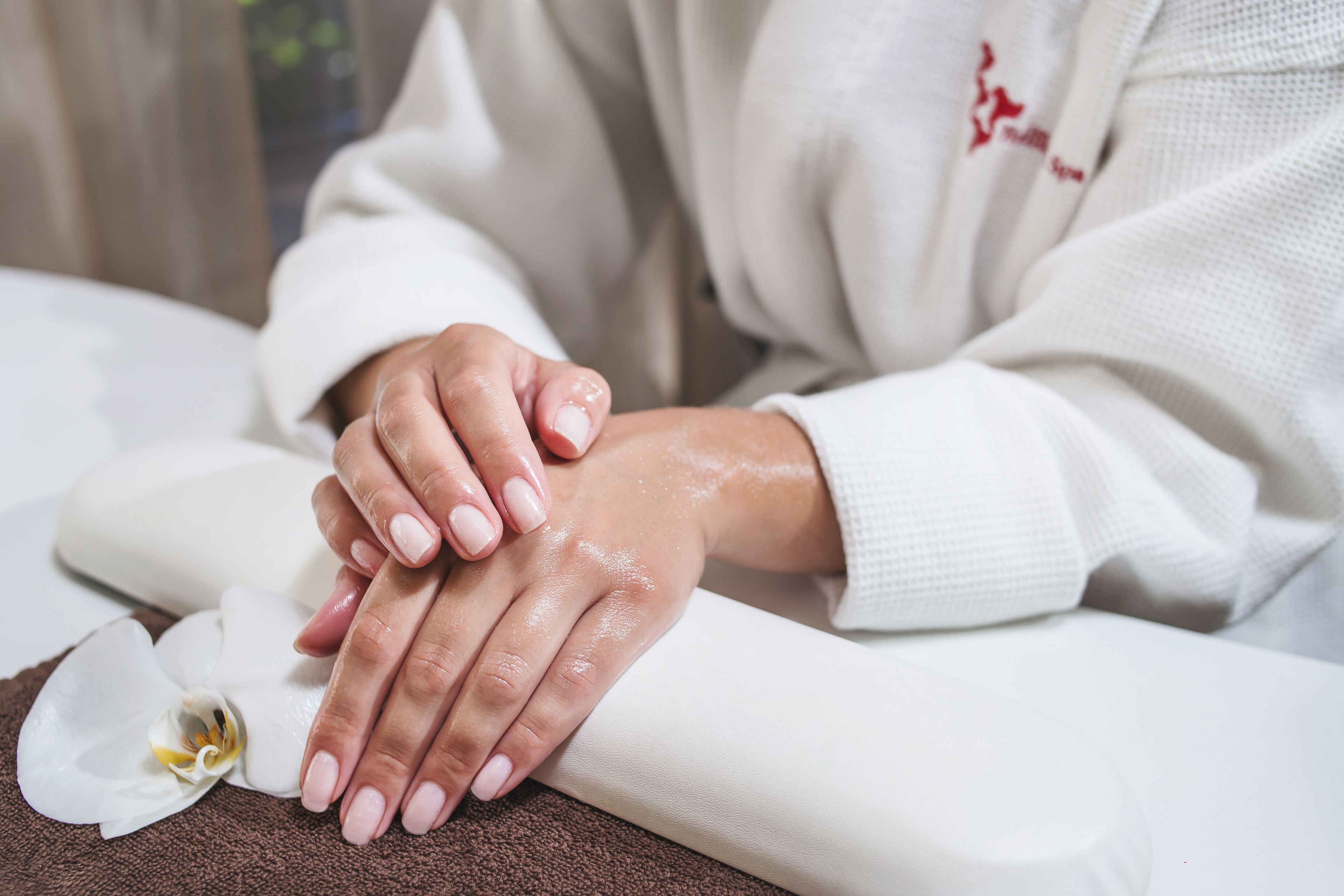 A close-up of hands resting on a towel, with a white flower nearby.