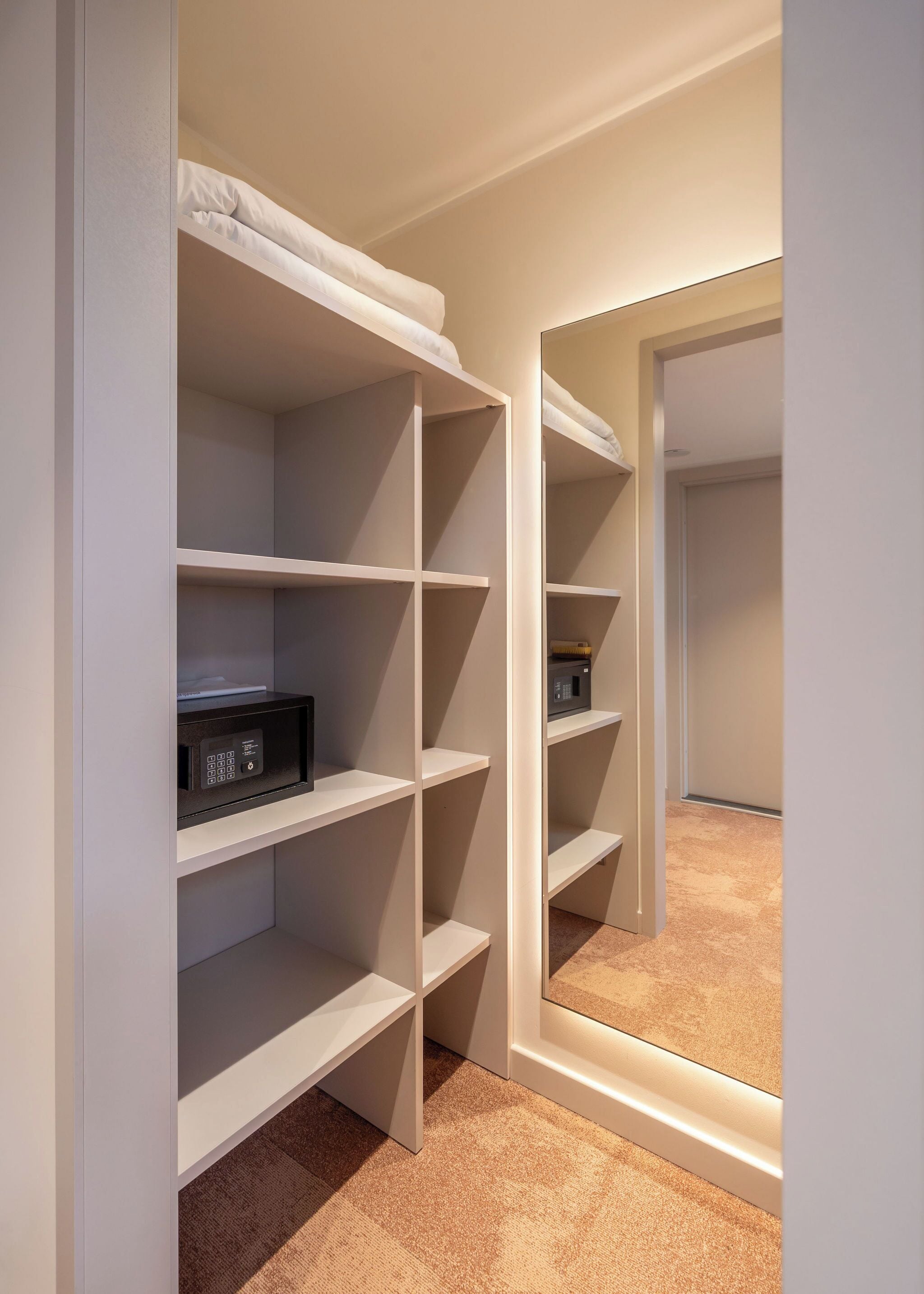 A walk-in closet with white shelving, a microwave on the bottom shelf, and a mirror on the right wall.